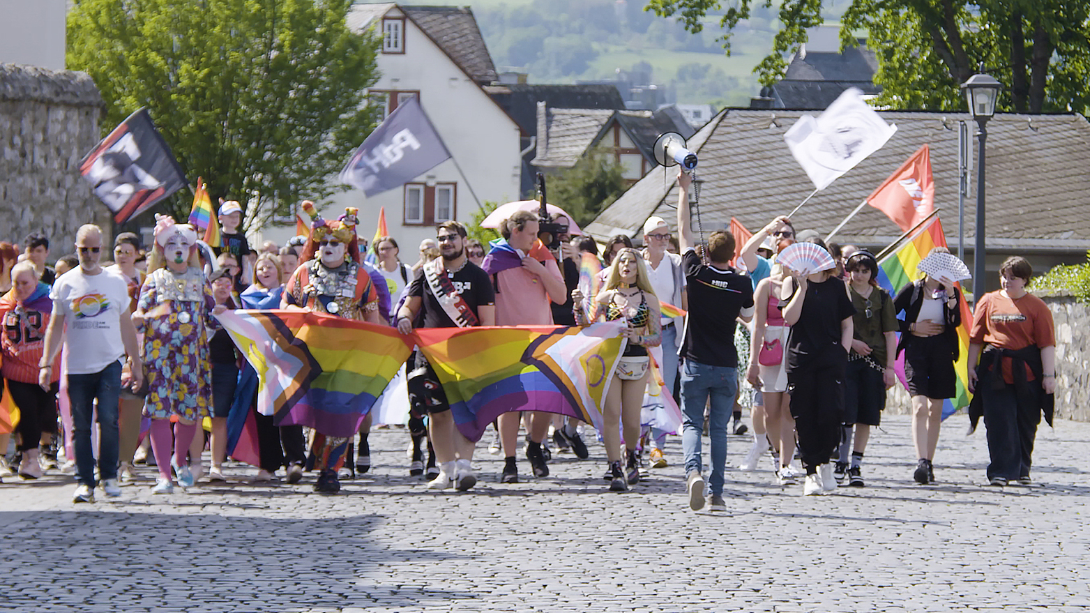 Eine Gruppe bunt gekleideter Menschen hält progress pride Flaggen in den Händen und demonstrieren auf dem Christopher Street Day für queere Sichtbarkeit.