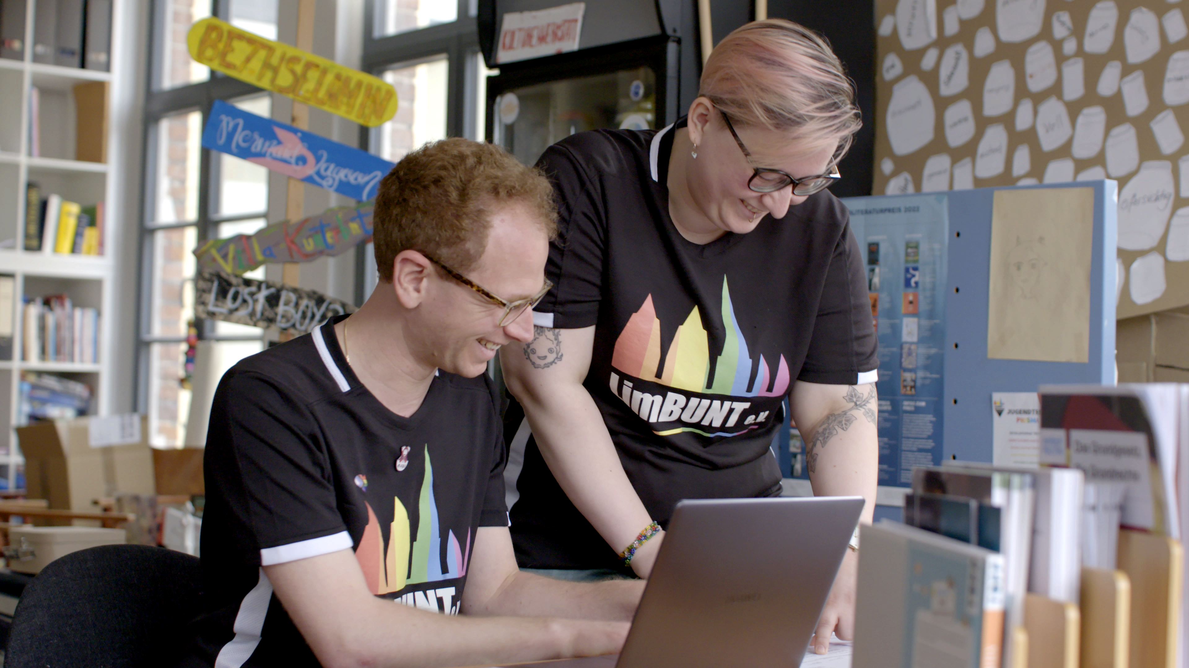 Es sind zwei Ehrenamtliche des Vereins LimBUNT e.V. zu sehen, die fröhlich ihrer Arbeit am Laptop nachgehen.