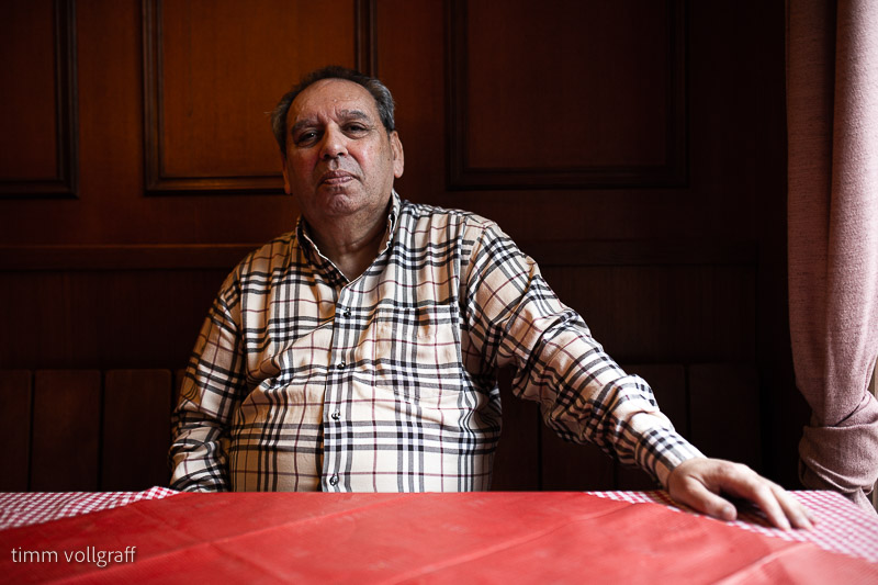 Ricardo Lenzi Laubinger sitzt an einem Tisch, der mit einer roten Tischdecke bedeckt ist und schaut ernst in die Kamera. Er trägt ein kariertes Hemd.