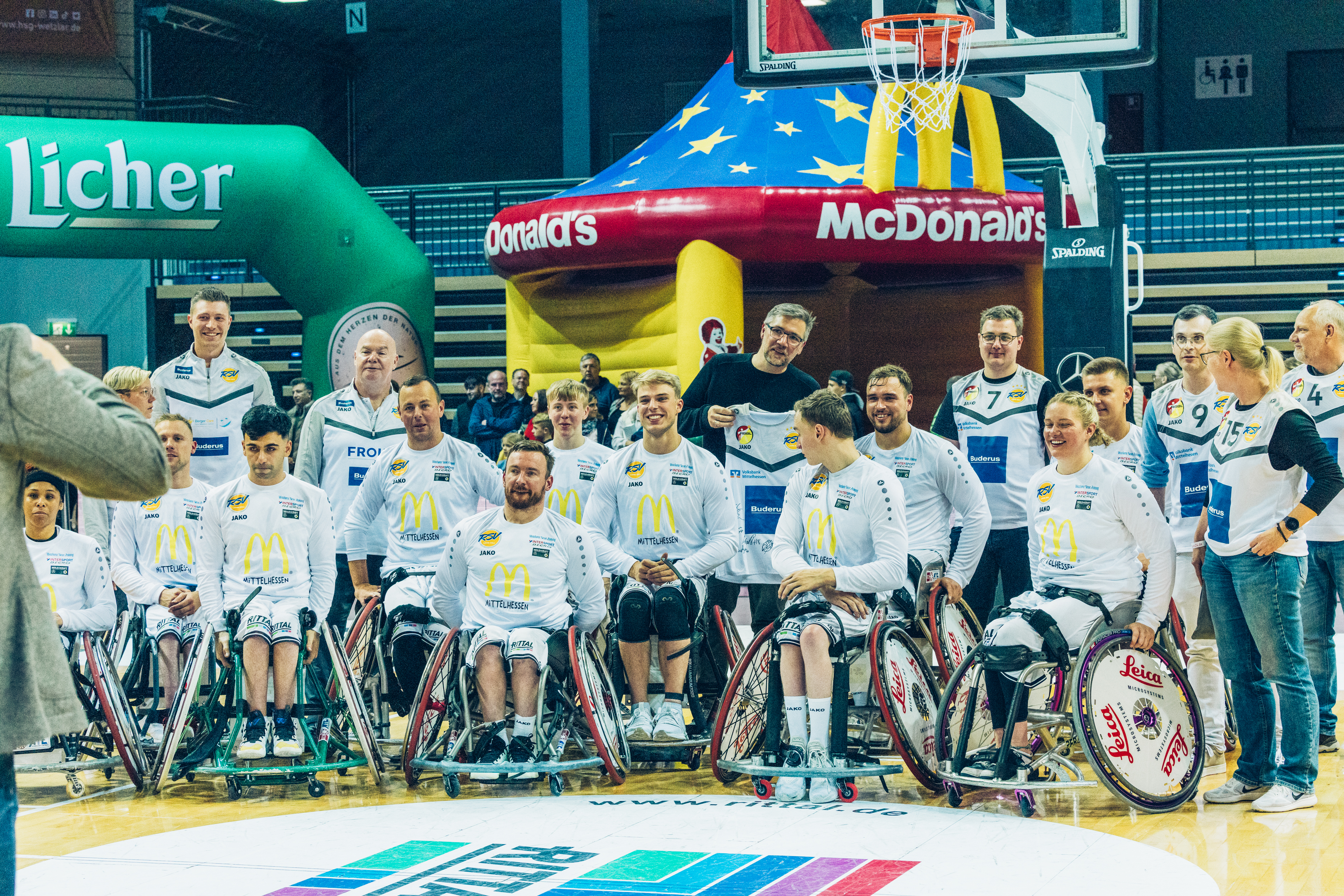 Gruppenbild des amtierenden deutschen Meisters im Rollstuhlbasketball RSV-Lahn-Dill nach ihrem Sieg in Wetzlar. Die Spieler:innen tragen weiße Trikots, hinter ihnen steht das Trainer:innen-Team.